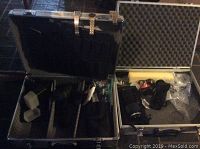 View of two large metal hard cases opened, showing camera accessories including lens, meter, and soft pouches.