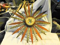 Front view of a retro starburst wall clock with alternating wooden and brass-tone rays surrounding the clock face.