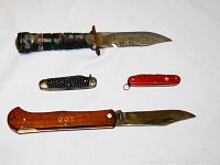 Four knives arranged on white background showing the survival knife, two folding knives and a Swiss Army style knife.