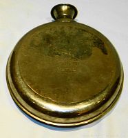 Front view of the vintage Gillette metal water bottle showing its round, flattened shape and tarnished metal surface with embossed text.