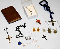 Multiple religious items laid out including crosses, rosaries, pendants, medals, and a small brown prayer book.