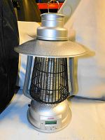 Close-up of silver portable bug zapper showing digital display, metal top with minor damage, and protective grid.