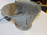 Front side view of metal coal bin showing curved top, metal handle, and wear marks