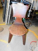 Front view of primitive wooden chair showing curved seat and flared backrest.