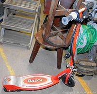 Side view of red and silver Razor electric scooter with foldable step deck and handlebar grips, showing Razor logo on deck.