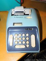 Full machine view showing keypad, paper roll, and overall blue casing.