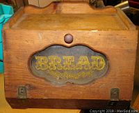 Front view of retro wooden bread box with glass front flap showing the word BREAD in yellow decorative lettering.
