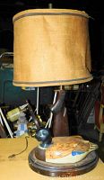 Full lamp showing fabric cylindrical shade and base with carved duck decoy body.