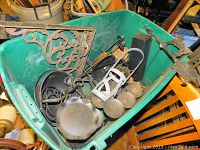 Photo showing a large collection of black metal items inside a green bin, including decorative wall brackets, candle holders, and metal rings.