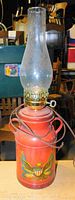 Full view of Americana hurricane lamp showing red base with eagle emblem, brass burner, and clear glass chimney.