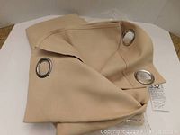 Close-up photo of beige drape fabric with visible metal grommet rings.