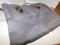 Close-up photo of folded gray drape panels showing metal grommets at the top.