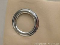 Close-up image of a single silver metal grommet against beige fabric.