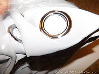 Close-up photo showing white fabric and silver grommets of the drape.