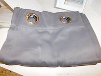 Folded gray drape panel featuring wide, silver metal grommets at the top for mounting on curtain rods.