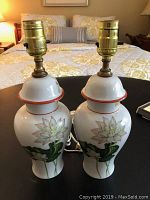 Pair of porcelain urn-shaped lamps on a black table with floral design and brass sockets