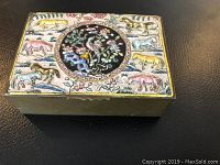 Oblique angled view of rectangular brass box with colorful horses and floral enamel design on top.