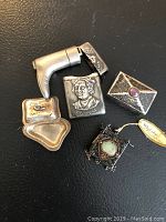 Photo showing five sterling silver miniatures including a boot, locket with face, small open box, envelope box and filigree box.