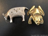 Two metal figurines, brass frog on right and pewter bull on left, showing size and detail on black surface.