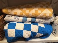 Stacked view of the three quilts partially folded showing the distinct colors and patterns for each quilt.