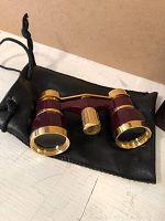 Small vintage binoculars with maroon body, gold rims and central focus knob, resting on black pouch