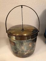 Front view of the silver plate ice bucket with lid and handle up, showing tarnished surface and metal finish.