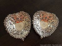 Two sterling silver heart-shaped footed dishes shown from top, displaying pierced and engraved monogrammed surface.
