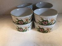 Group of 8 porcelain custard dishes stacked showing floral decoration on sides and round shape.