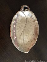 Full view of silver leaf-shaped dish on dark surface