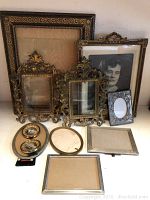 Full lot of eleven antique frames in various ornate styles, gold-toned and silver-toned metals, and wood, displayed on table against a light wall