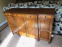 Front view of antique wooden sideboard showing three drawers and cabinet doors under natural light.