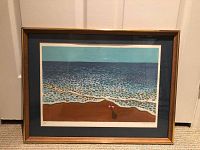 Framed lithograph print of beach with ocean waves and figure visible, in wooden frame and blue matting.