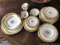 Full view of stacked dinnerware plates, bowls, and tea cups with floral embossed design and gold trim.