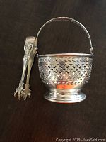 Photo showing the sterling silver basket with a handle and attached ornate sugar tongs hanging from the basket handle.
