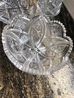 Top view of a round cut crystal bowl featuring star and diamond patterns with a scalloped rim, showing clear intricate cuts and chips on the edge.