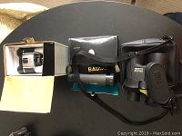 Three pairs of binoculars with cases and boxes arranged on black table