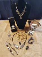 Full view of lot including antique vanity mirror, necklace on black bust, watches, bracelets, and various jewelry pieces arranged on table.
