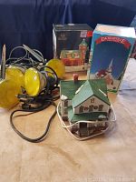Photo of two Dickensville collectible houses with their original boxes and four yellow spotlights with cords on a surface.