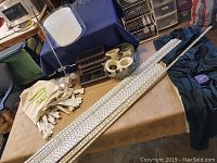 Wide view of bag containing different metal shelving brackets of various sizes, air registers, and pot light covers arranged on table with cloth and chairs in background.