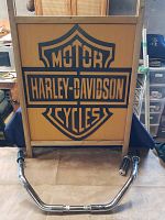 Full frontal view of wood framed Harley-Davidson logo sign with chrome ape hanger handlebars below it