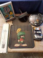 Lot includes Marvin the Martian floor mat, Simpsons Moe's Tavern artwork, metal wall thermometer, round wall clock, dumbbell, and packaged UFC training gloves
