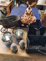 Full shot of vintage pram, rabbit figure, metal buckets, lanterns, and car organizer on table