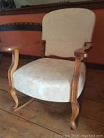 Full view of the antique rocking chair showing the wooden frame and newly reupholstered light beige seat and backrest.