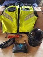 Front view of the hi vis safety vest, black motorcycle helmet, leather clutch purse, and fabric accessories laid out