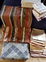 Photo showing brown striped king size duvet cover and pillow shams folded, with additional beige pillowcases and a grey patterned fabric item on dark surface