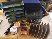 Overview of all items in the lot on wooden table, including vintage and newer file holders, hole punch, staplers, and DVDs