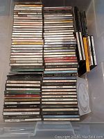Photo of the collection of 90 CDs stacked in plastic bin showing jewel cases and spines with artist and album names.