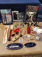Photo showing various items including antique oil can, tire pressure gauge, magnetic mesh screen door, beer can chicken holder, Snap-On flashlight, Ford emblems, and other miscellaneous items on blue background.