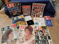 Photo showing collection of vintage magazines including LIFE, LOOK, and Rolling Stone, with visible covers featuring Liz Taylor and Jacqueline Kennedy, plus collector coin set boxes and stamp covers.