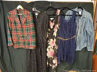 Lot of 5 clothing items including plaid jacket, three dresses, and denim shirt hanging on a black background.